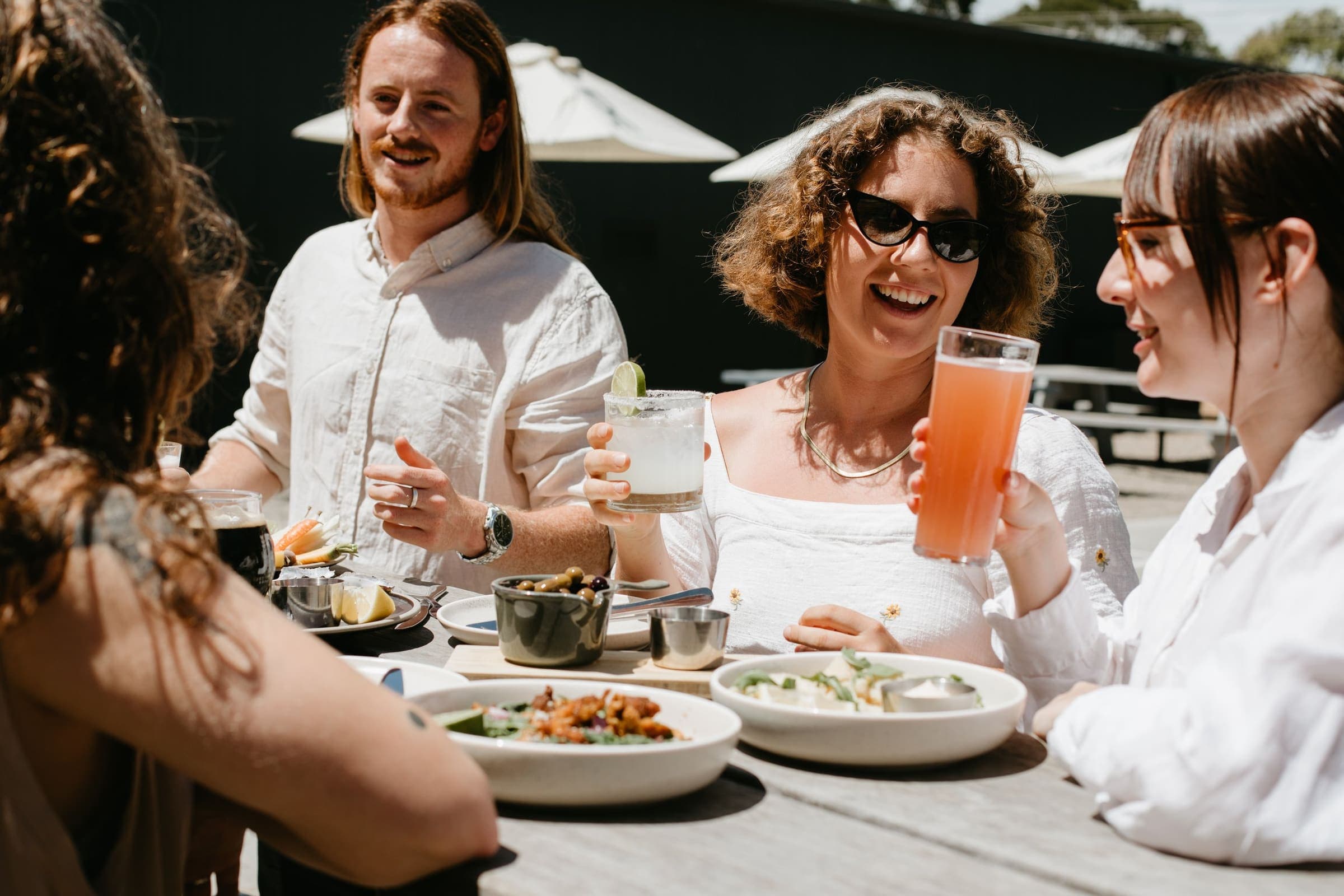 Friends sharing plates and drinks at a sunny beer-garden table